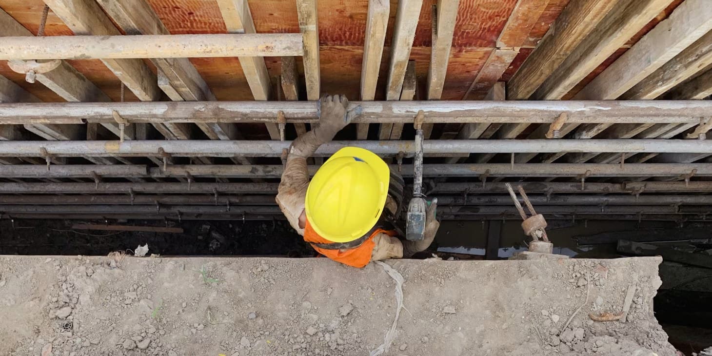 Overhead view of a construction worker in a yellow hard hat working under a slab