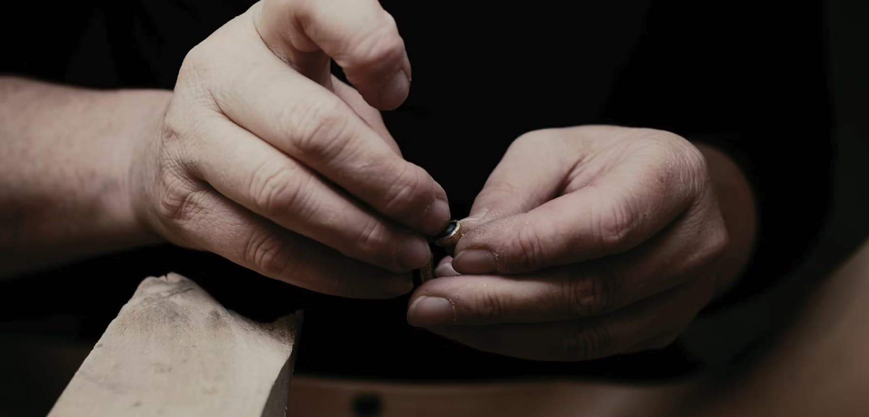 Close-up of a craftsman's hands setting a small gold piece at a wooden bench