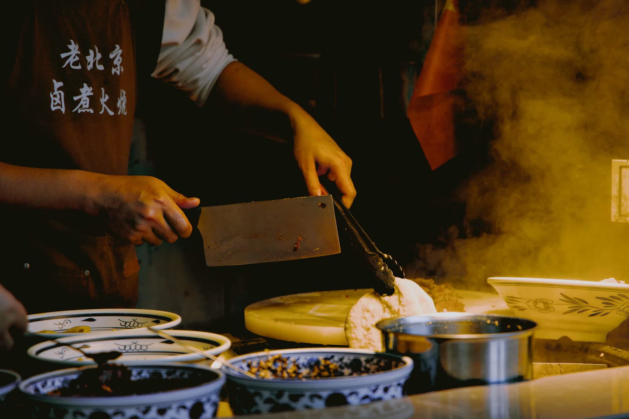 A chef working a cleaver over a steaming kitchen line