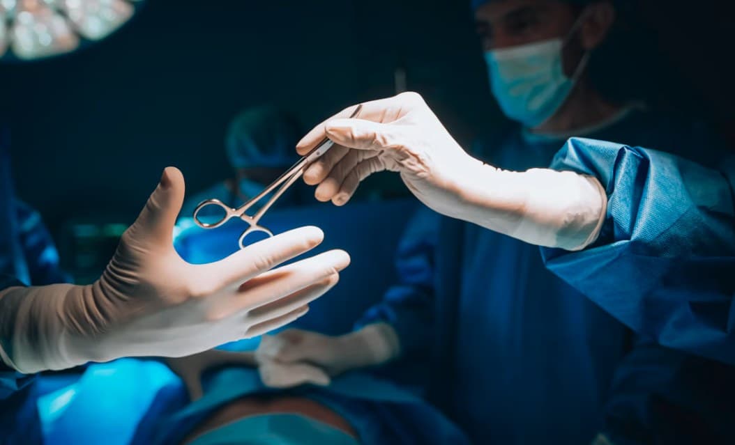 A gloved surgeon passing forceps across an operating table